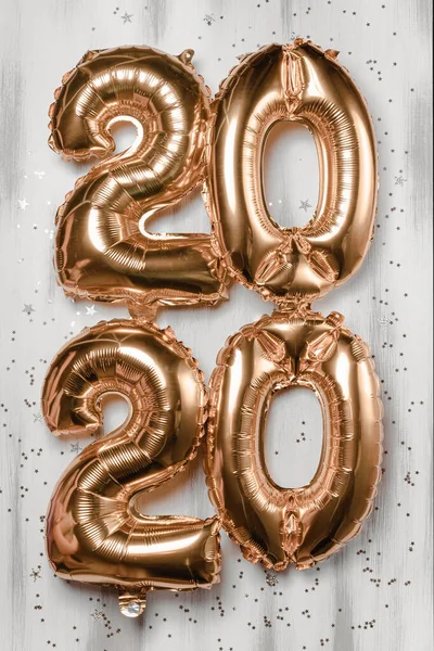 Happy New year 2020 celebration. Bright gold balloons figures, New Year Balloons with glitter stars on wood white background. Christmas and new year celebration. Gold foil balloons 2020