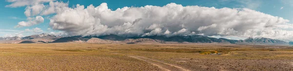 Panorama of desert landscape on background snow-capped mountain peaks. View Mountain in with peaks in the clouds . Autumn landscape