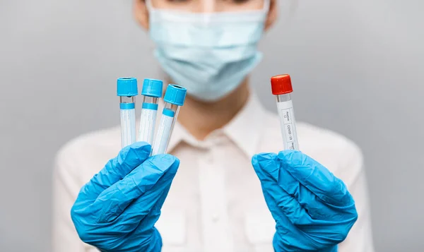 Κορίτσι Γιατρός σε ιατρική μάσκα και γάντια καουτσούκ, κρατά στα χέρια της, closeup του σωλήνα δοκιμής με δοκιμές για την παρουσία του covid-19. Γιατρός με ιατρικά ρούχα επιδεικνύει δοκιμαστικούς σωλήνες με coronavirus — Φωτογραφία Αρχείου