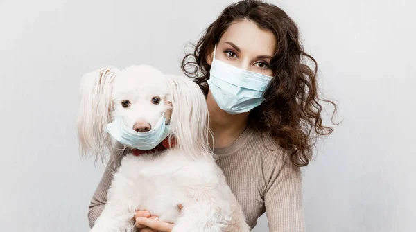 Vrouw in beschermende chirurgische masker houdt hond huisdier in gezichtsmasker. Coronavirus COVID-19 is gevaarlijk voor huisdieren. Meisje met medisch masker en hond met beschermend masker. Voorzorgsmaatregelen tegen coronavirus — Stockfoto