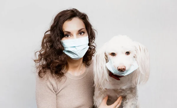 Vrouw in beschermende chirurgische masker houdt hond huisdier in gezichtsmasker. Coronavirus COVID-19 is gevaarlijk voor huisdieren. Meisje met medisch masker en hond met beschermend masker. Voorzorgsmaatregelen tegen coronavirus — Stockfoto