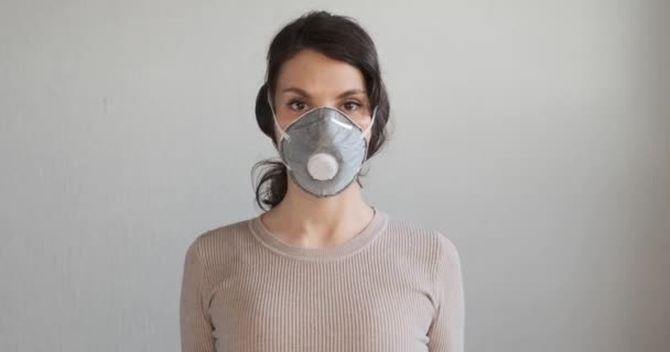 Молодая женщина показывает, как носить защитную медицинскую маску. Красивая девушка показывает защитную маску во время пандемии. Здравоохранение и медицинское понятие. Закрыть портрет девушки в защитной маске — стоковое видео