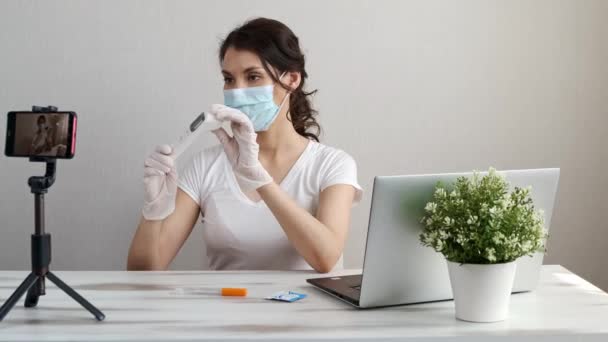 Influencer Girl blogger in medical mask talks about coronavirus. Woman recording video blog tells how to protect yourself from covid 19. Bloger talks mers-cov how to use of alcohol wipes,thermometer — Stock Video