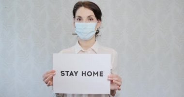 Tıbbi maskeli genç bir kız, evde olduğu için, doktorlara yardım etmesi için baskı yapıyor, üzerinde yazı olan posteri gösteriyor, evde kalıyor. Eldivenli kadın yazıyı gösterdi, lütfen doktorlara yardım edin, evde kalın.