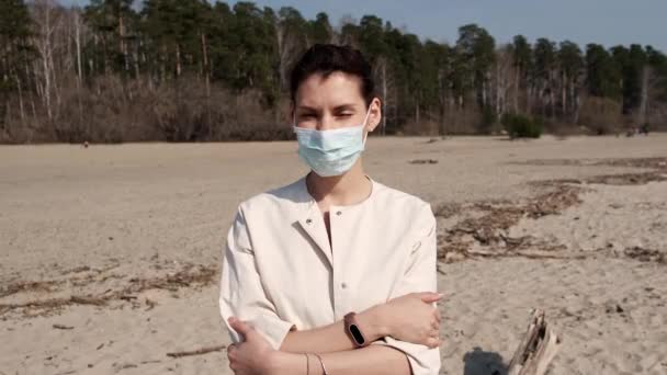 Young girl in medical mask, being outdoors during quarantine during pandemic covid-19, looking at the camera. Masked woman on outdoors. Need to stay home. Lady walking in public space on quarantine — Stock Video