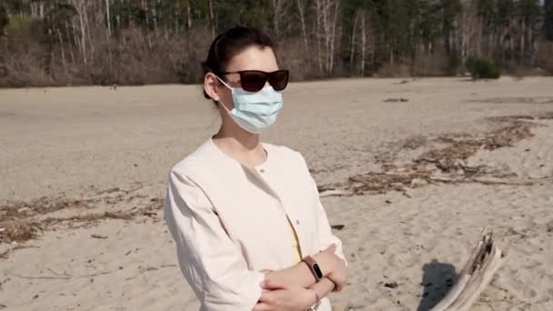 Young girl in medical mask, being outdoors during quarantine during pandemic covid-19, looking at the camera. Masked woman on outdoors. Need to stay home. Lady walking in public space on quarantine — Stock Video