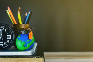 Eğitim konsepti - kitaplar, çalar saat, kil toprak, masanın üzerindeki tebrik şapkası.