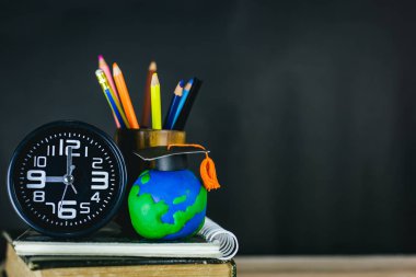 Eğitim konsepti - kitaplar, çalar saat, kil toprak, masanın üzerindeki tebrik şapkası.