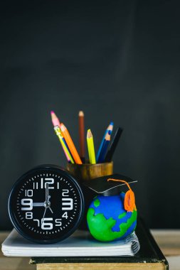 Eğitim konsepti - kitaplar, çalar saat, kil toprak, masanın üzerindeki tebrik şapkası.