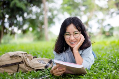 Asyalı bir üniversite öğrencisinin portresi ya da gözlük takan liseli bir kızın üniversitede ağacın altında fotokopi alanı olan kitaplar okuması. Eğitim ve inek zeki insanlar konsepti.
