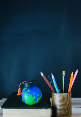 Eğitim konsepti - kitaplar, çalar saat, kil toprak, masanın üzerindeki tebrik şapkası.