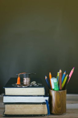 Eğitim konsepti - kitaplar, çalar saat, kil toprak, masanın üzerindeki tebrik şapkası.