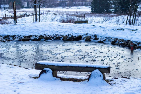 Un banco de madera cubierto con un poco de hielo en el lago Eugenisee de Engelberg pueblo y hermosos paisajes con nieve, el sol brillante y las montañas en invierno, invierno en Suiza — Foto de Stock