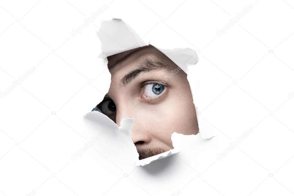 Man With Blue Eyes Looking Through White Ripped Paper Hole