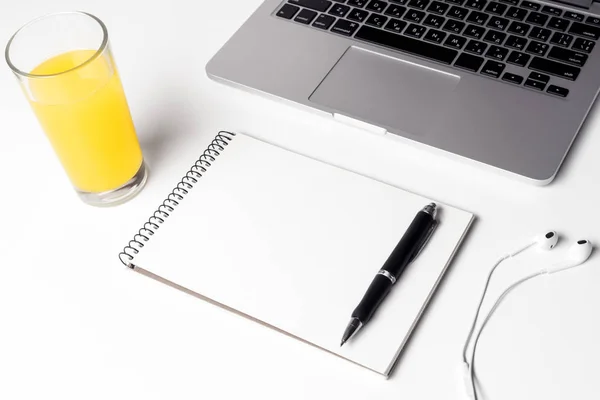 Vetro con succo, notebook con penna e cuffie vicino al computer portatile — Foto Stock