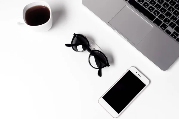 Tazza con caffè, occhiali da sole e smartphone vicino al computer portatile — Foto Stock