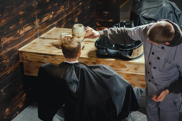 小さな男の子は 理髪店の椅子に座りながら床屋で散髪を取得します 理髪店のテーマ ストック写真