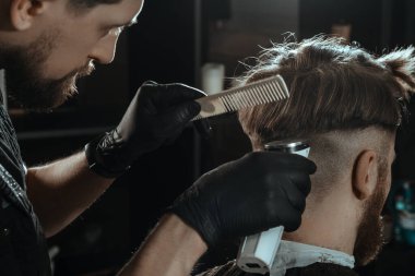 BARBERshop teması. Koyu renk eldivenli BARBER GERÇEK KÜÇÜK KÜLTÜKLERİNİ TÜRÜNÜYOR. O bir saç kesicisi kullanıyor.