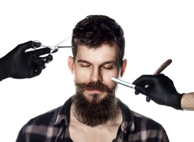 Beyaz arka planda kareli gömlekli, uzun sakallı ve kapalı gözlü yakışıklı bir adam. Berber dükkanı teması. Siyah eldivenli berberin elleri bir jilet ve bir adamın yüzüne yakın bir makas tutuyor.