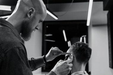 BARBERshop teması. Kel Barber, sakallı, ciddi müşterisinin saçlarını kesiyor. - Kel mi? O bir saç kesicisi kullanıyor.