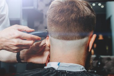 BARBERshop teması. BARBER, Bıyıklı müşterisinin saçlarını kesmeye çalışıyor. O bir saç kesicisi kullanıyor.