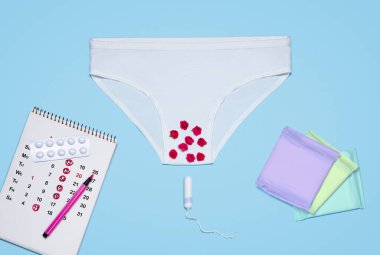 white wooman pants near calendar, tablets, tampon and menstrual pads on a blue background. critical days. menstruation them clipart