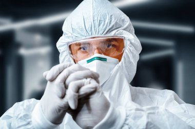 Concentrated scientist in protective suit  and a medical respirator stretching hands in rubber gloves in laboratory. Covid-19 outbreak concept. Coronavirus epidemic theme clipart
