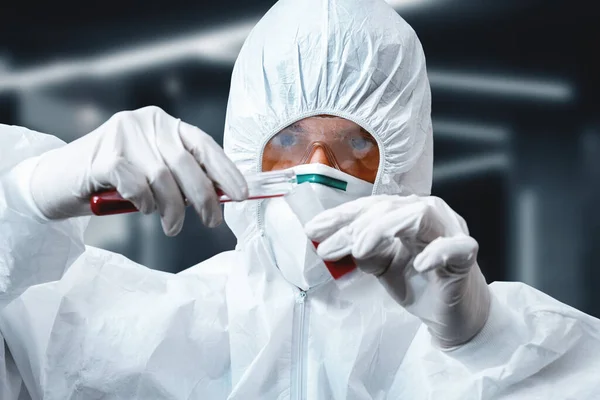 Concentrated scientist in protective suit with test tubes in hands for covid-19 virus in laboratory. Covid-19 outbreak concept. Coronavirus epidemic theme