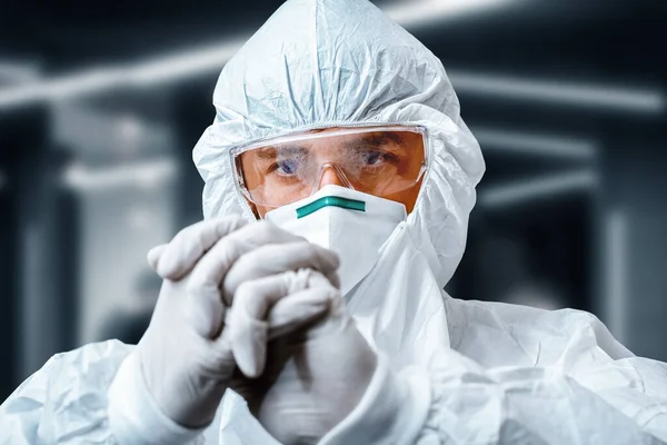 Concentrated scientist in protective suit  and a medical respirator stretching hands in rubber gloves in laboratory. Covid-19 outbreak concept. Coronavirus epidemic theme