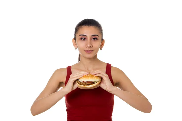 Szép, fiatal lány a tréningruhaként egy hamburger kezében elszigetelt fehér background — Stock Fotó
