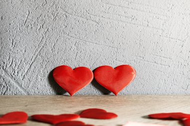 İki kırmızı kalp, ahşap bir masanın yanında dokulu bir duvara karşı durur. Diğer kalpler masaya saçılmış.