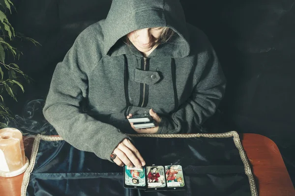 fortune telling on tarot cards. at the table, a witch in a gray hoodie makes a layout with tarot cards