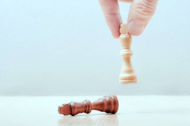 El masaya bir satranç kotolünün beyaz parçasını koyar. Masanın üzerinde mağlup siyah kral yatıyor. iş başarısı konsepti