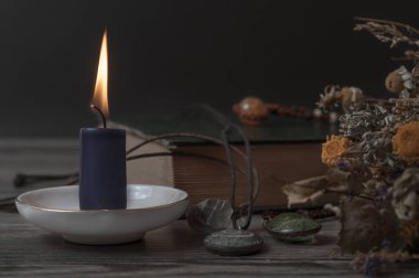 Yanan bir mum, bir kitap, kuru otlar ve sihirli taşlar. Cadılar için ayarlandı.