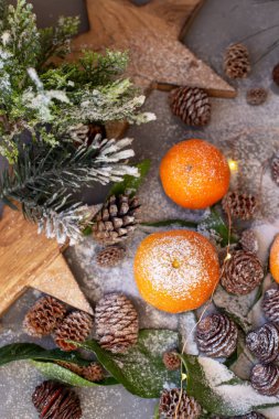 Gri arka planda turuncu mandalinalar. Kahverengi kozalaklı ve yeşil yapraklı yeni yıl dekorunda. Mandalinalı Noel süsü. Lezzetli tatlı Clementine.