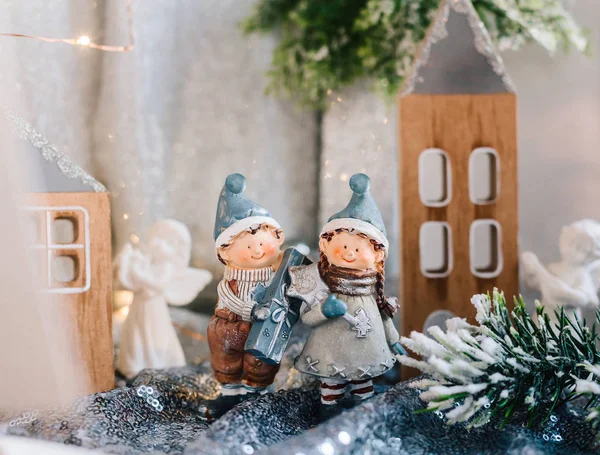 Noel dekoru içindeki çocukların porselen figürleri. Evlerin ve konilerin arka planında hediyeleri olan bir erkek ve bir kızın kış figürleri. Noel tebrik kartı. Boşluğu kopyala.