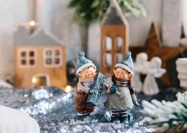 Noel dekoru içindeki çocukların porselen figürleri. Evlerin ve konilerin arka planında hediyeleri olan bir erkek ve bir kızın kış figürleri. Noel tebrik kartı. Boşluğu kopyala.