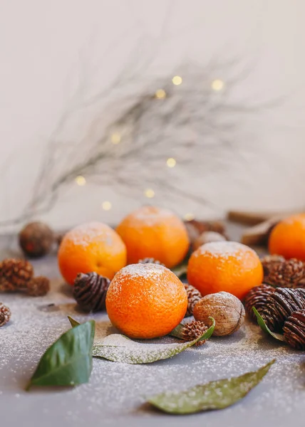 Orangefarbene Mandarinen auf grauem Hintergrund im Neujahrsdekor mit braunen Tannenzapfen und grünen Blättern. Weihnachtsdekoration mit Mandarinen. leckere süße Clementine. — Stockfoto