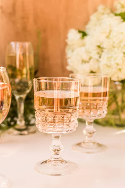 Gözlüklü gül kırmızısı şarap. Arka planda çiçekler olan bir şişe gül şarabı. Prosecco.