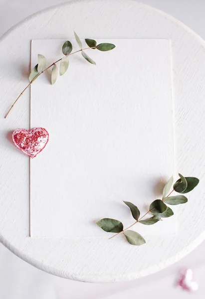 Bakgrund med kopia utrymme tomt på vitt bord med glitter hjärta, eukalyptus gren, blommor och blad. Vit papper ovanifrån, platt låg, minimal stil. Uppblåst kort. — Stockfoto