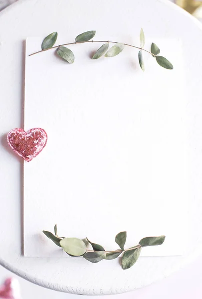Background with copy space blank on white table with glitter heart, eucalyptus branch, flowers and leafs. White paper top view, flat lay, minimal style. Moke up card. — Stock Photo, Image