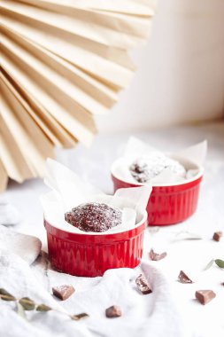 Kırmızı bardakta çikolatalı kek. Gri ve beyaz arka planda kahverengi kekleri olan küçük seramik ramekin..