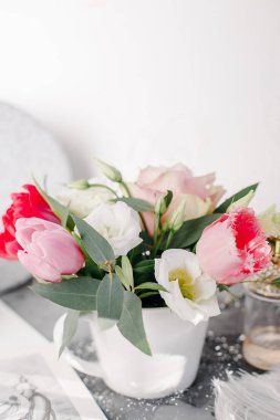 Spring bouquet in white vase on wooden white stand. Roses, tulips and lisianthus.