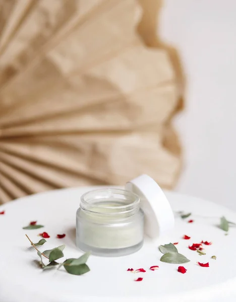 Powder cosmetic mask. Glass jar with matcha on a white background with dry petals.
