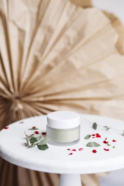 Powder cosmetic mask. Glass jar with matcha on a white background with dry petals.