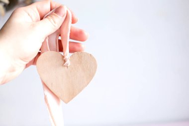 Beyaz arka planda açık ahşap bir kalp ve ipek pembe kurdele. Mesaj için yer var. Soluk pembe bir kurdelenin üzerinde tahta bir kalp kolyesi tutuyor. Boşluğu kopyala.