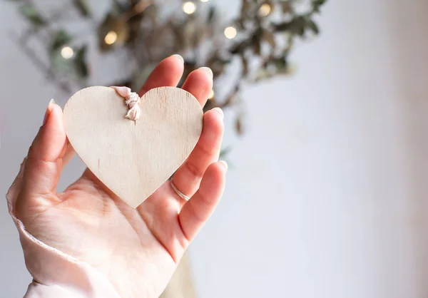 Licht houten hart op een zijden roze lint op witte achtergrond. Ruimte voor tekst. Hand met een houten hart hanger op een chiffon lichtroze lint. Kopieerruimte. — Stockfoto