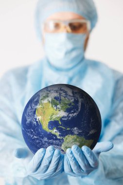 Doktor elini toprağı tutarken yaklaş. Model yap. Tıbbi ekipman. COVID 19 Coronavirus enfeksiyonunu korumak için maske, gözlük ve giysi de dahil olmak üzere kişisel koruyucu ekipman giyen bir doktor..