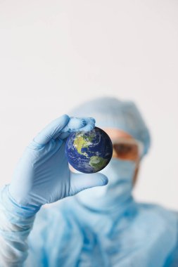 Doktor elini toprağı tutarken yaklaş. Model yap. Tıbbi ekipman. COVID 19 Coronavirus enfeksiyonunu korumak için maske, gözlük ve giysi de dahil olmak üzere kişisel koruyucu ekipman giyen bir doktor..