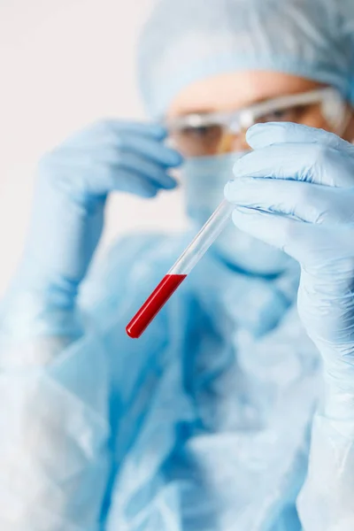 Kan örneğini tutan doktorun eline yaklaş. Tıbbi ekipman. Kan testi. COVID 19 Coronavirus enfeksiyonunu korumak için maske, gözlük ve giysi de dahil olmak üzere kişisel koruyucu ekipman giyen bir doktor..